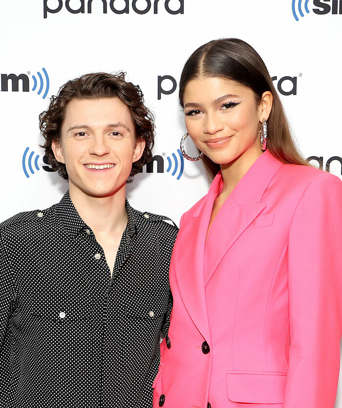 Zendaya smiling in a bright pink blazer at a media event, with fans speculating pregnancy after photo with Lisa.