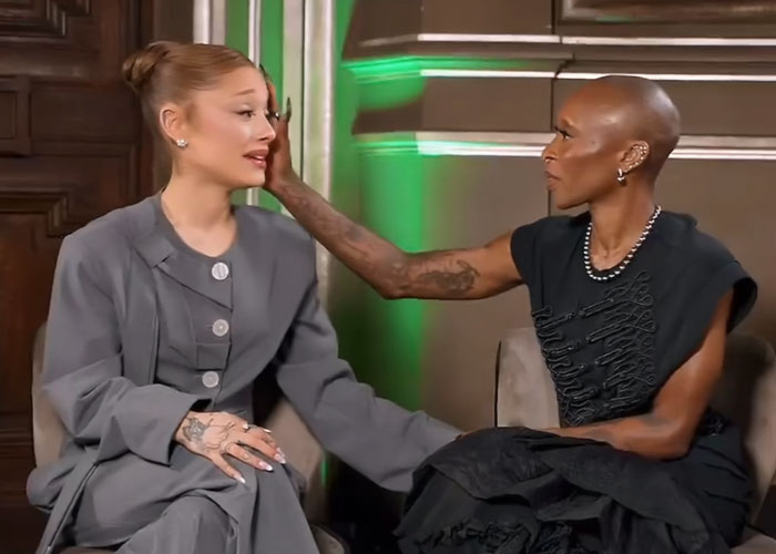 Ariana Grande and Cynthia Erivo seated and interacting during a candid moment amid interview discussions.