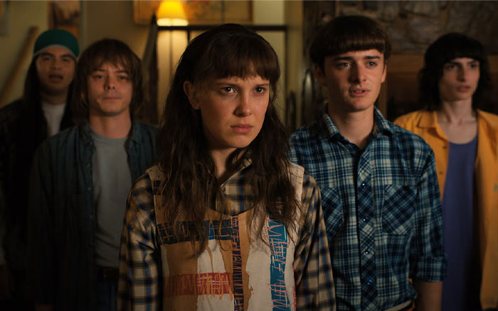 Five Stranger Things actors in casual 1980s-style clothing standing indoors, portraying intense emotions in a dramatic scene. Five Stranger Things actors in casual 1980s-style clothing standing indoors, portraying intense emotions in a dramatic scene.