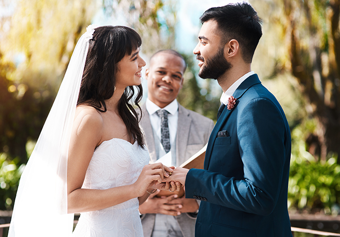 Bride and groom exchanging rings during outdoor wedding ceremony with officiant, capturing spiritual bride&rsquo;s emotional moment.