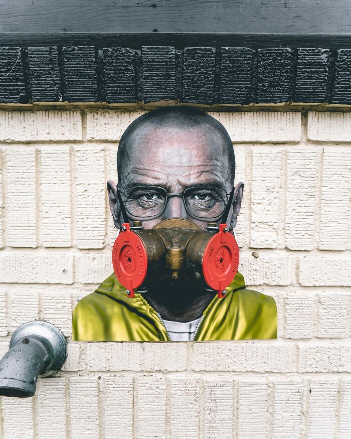 Paper cutout of a man wearing glasses and a gas mask, perfectly integrated with real life on a brick wall.