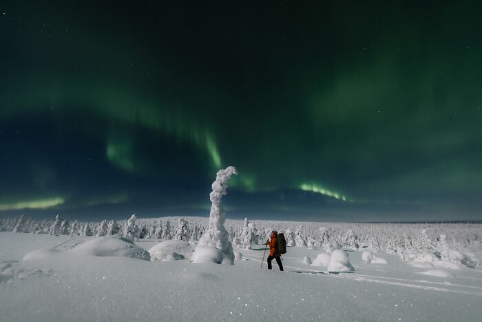 Person hiking in snowy landscape under green Northern Lights, showcasing one of the best places and times to see the Northern Lights.