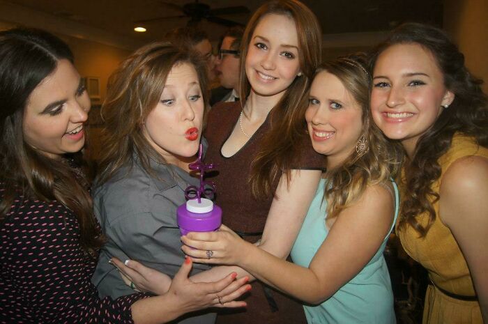 Five young women smiling and posing closely together at a party, capturing an epic photobomb moment.