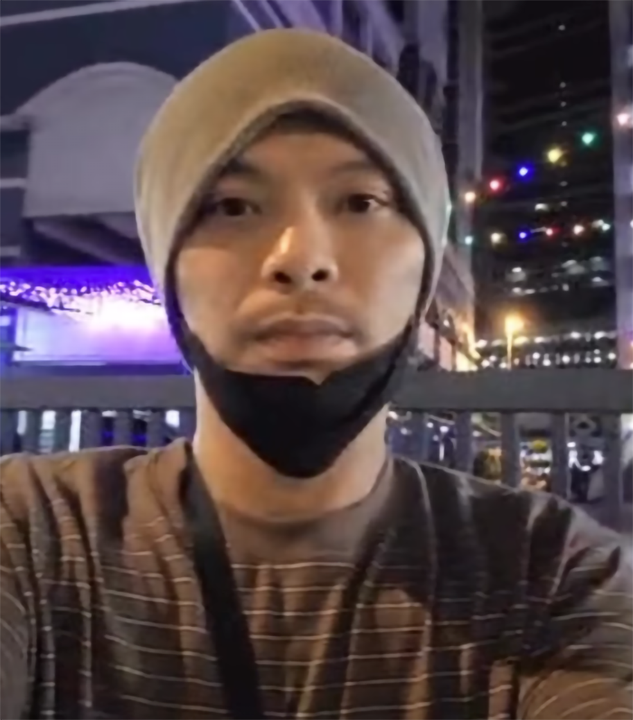 Man wearing a beanie and lowered mask outside at night in a city setting with colorful lights in the background Man wearing a beanie and lowered mask outside at night in a city setting with colorful lights in the background