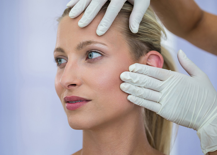 Woman undergoing consultation for plastic surgeries, doctor examining her face with gloved hands in a clinical setting
