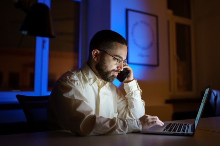 Man prioritizes work late at night, talking on phone and using laptop, ignoring family life and personal time. Man prioritizes work late at night, talking on phone and using laptop, ignoring family life and personal time.