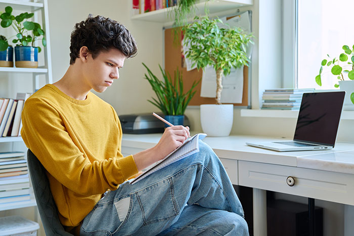 Teen writing at desk by laptop, symbolizing the gift of having his eyes opened and reality check to father.
