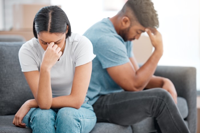 Man and woman sitting apart on sofa, both appearing stressed and upset, highlighting family and work conflict. Man and woman sitting apart on sofa, both appearing stressed and upset, highlighting family and work conflict.