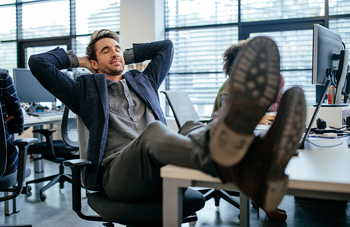 Employee relaxing at desk, deciding to stop overworking after doing the roles of multiple people in an office setting.
