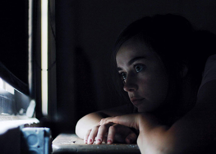 A young woman staring intently at a screen in a dark room, reflecting the fear of terrifying things found online.