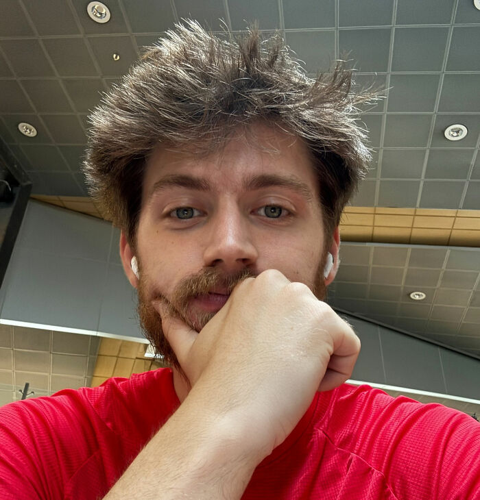 Young American travel influencer wearing red shirt and wireless earbuds, sharing footage of marathon experience in North Korea.