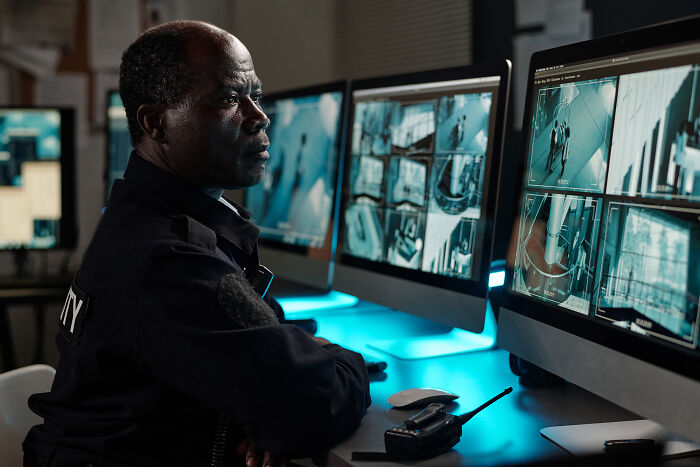 Security guard monitoring multiple surveillance camera feeds in a dimly lit control room focused on potential threats.