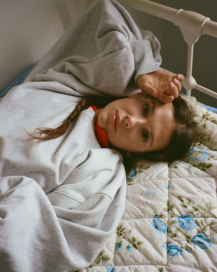 Millie Bobby Brown lying on a bed with gray sweatshirt, reflecting amid criticism about adopting a baby at 21. Millie Bobby Brown lying on a bed with gray sweatshirt, reflecting amid criticism about adopting a baby at 21.