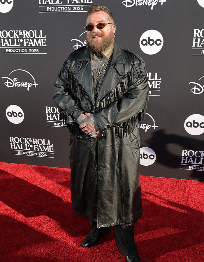 Person wearing a long black leather fringe coat and sunglasses posing on the red carpet at Rock Hall of Fame 2025.