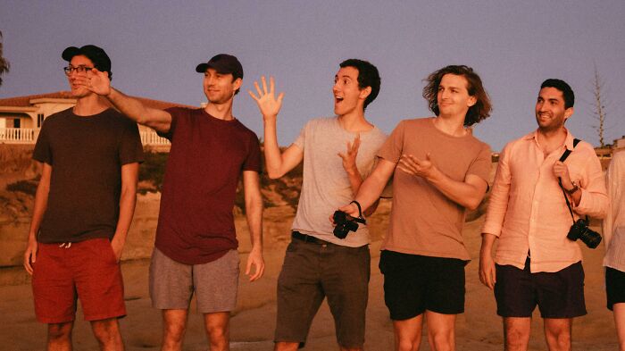 Group of young men outdoors at sunset, smiling and gesturing, illustrating relationship gestures and social interaction.