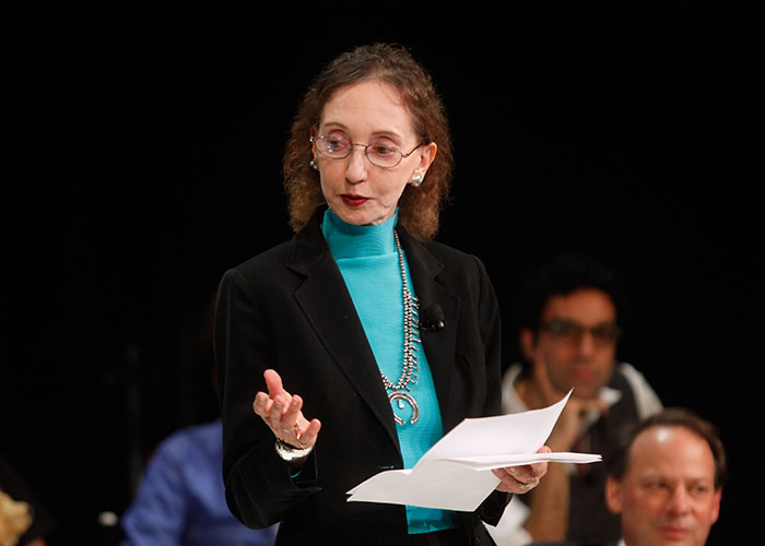 Joyce Carol Oates speaking at an event, wearing glasses and a black blazer, addressing Elon Musk criticism and uncultured comment.