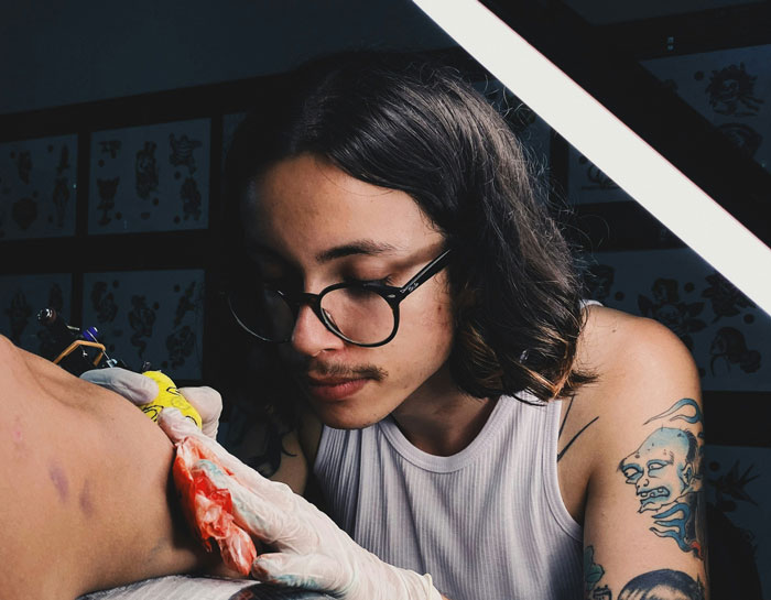 Tattoo artist focused on creating a detailed ink design while funny patients’ comments lighten the hospital and clinic vibe.