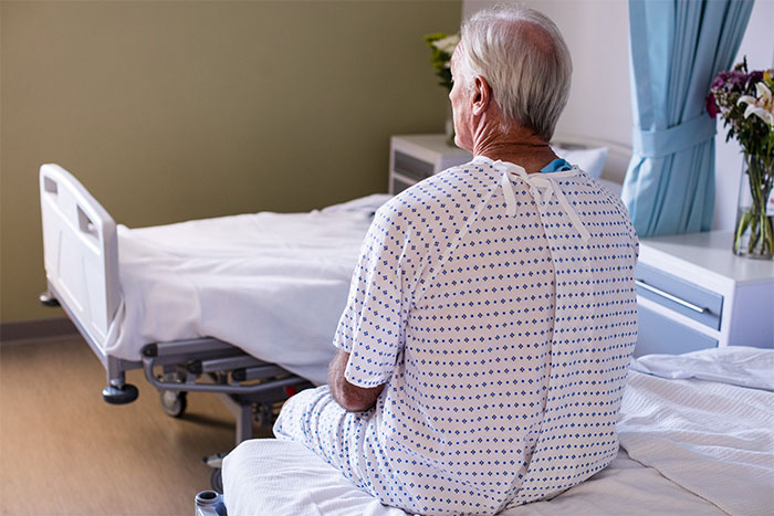Elderly patient in hospital gown sitting on bed in a quiet hospital room, evoking eerie moments patients said to doctors.