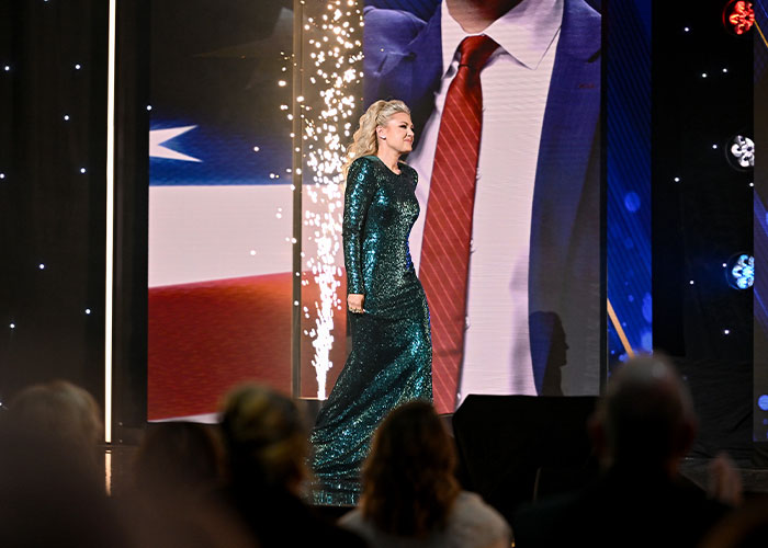 Erika Kirk walking on stage in a sparkling green dress, gestures sparking wild conspiracy theories about her acting.