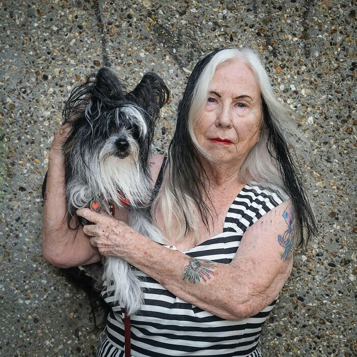 Elderly woman with half black and half white hair holding a dog with matching black and white fur, showing pets and humans resemblance.