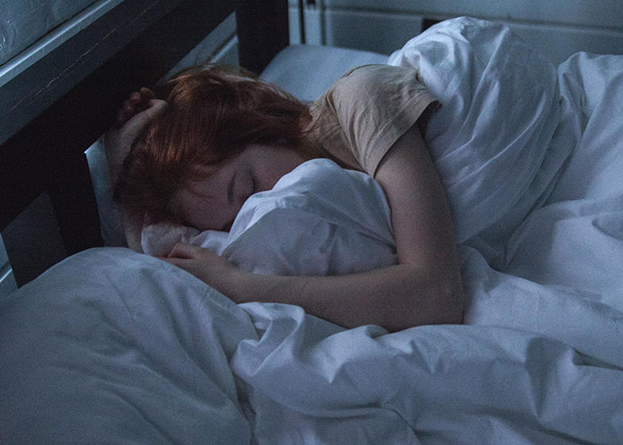 Woman resting in bed at night, wrapped in white sheets, evoking eerie and bizarre events that creep people out.