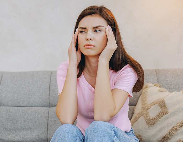 Woman feeling hurt and upset sitting on a couch, reflecting on partner&rsquo;s first birth support experience without her