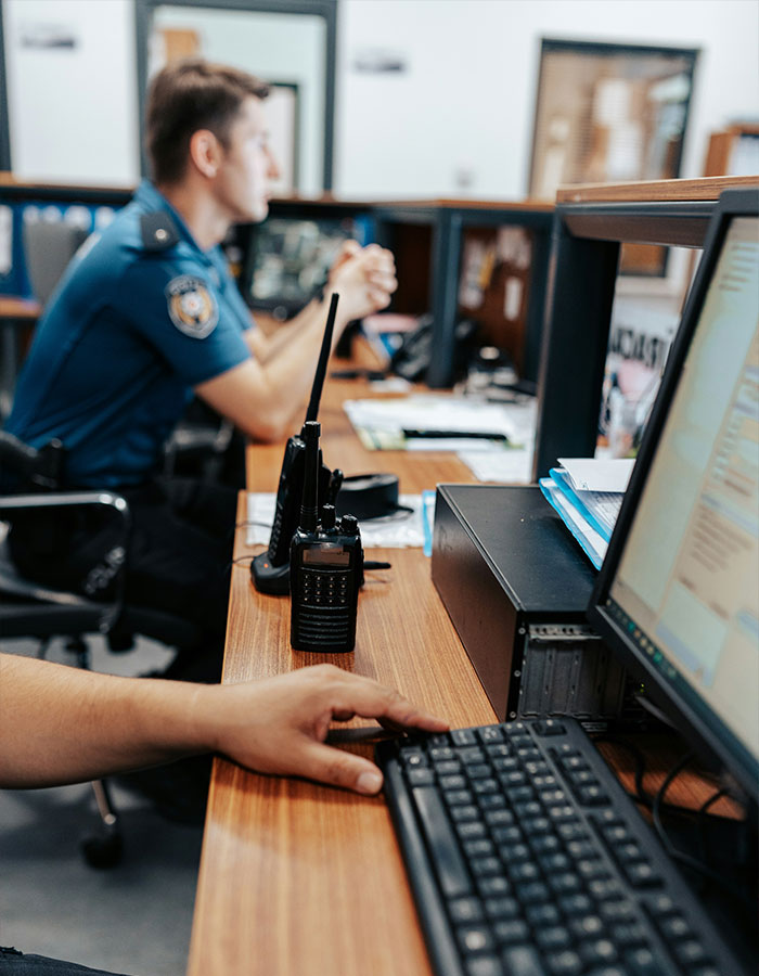 Police officers working at desks in station, featuring radio communication device and computer keyboard in focus. Police officers working at desks in station, featuring radio communication device and computer keyboard in focus.