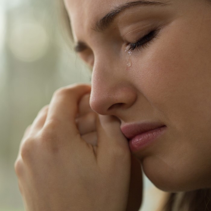 Close-up of a woman crying with tears on her cheek, reflecting emotional pain over family and work priorities. Close-up of a woman crying with tears on her cheek, reflecting emotional pain over family and work priorities.