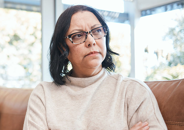 Woman wearing glasses, looking upset and thoughtful indoors, reflecting tension around Thanksgiving and family issues.
