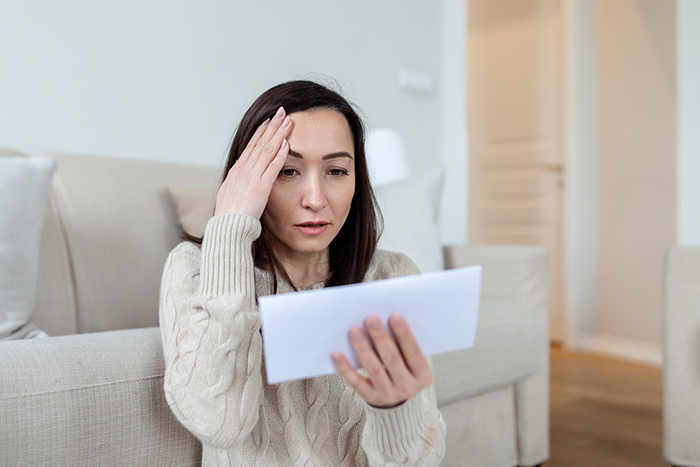 Woman in beige sweater looking worried while reading a letter, reflecting on relationship and breakup issues.