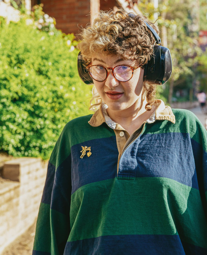 Person with curly hair and glasses wearing headphones outdoors, appearing thoughtful during dinner with mom’s boss. Person with curly hair and glasses wearing headphones outdoors, appearing thoughtful during dinner with mom’s boss.