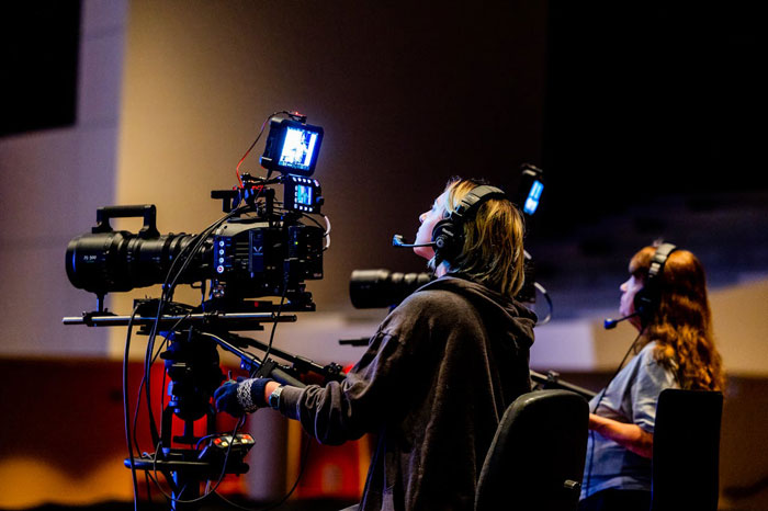 Cameraperson operating professional video camera with headset, capturing footage for modern movies in a studio setting.