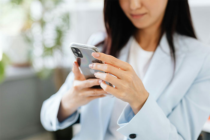 Woman holding smartphone, dressed in light blue blazer, appearing focused while texting about Friendsgiving dress-code betrayal. Woman holding smartphone, dressed in light blue blazer, appearing focused while texting about Friendsgiving dress-code betrayal.