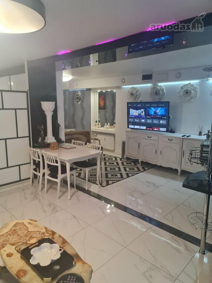 Modern living room and dining area with white furniture, patterned rug, and flat-screen TV in wild real estate listings interior.