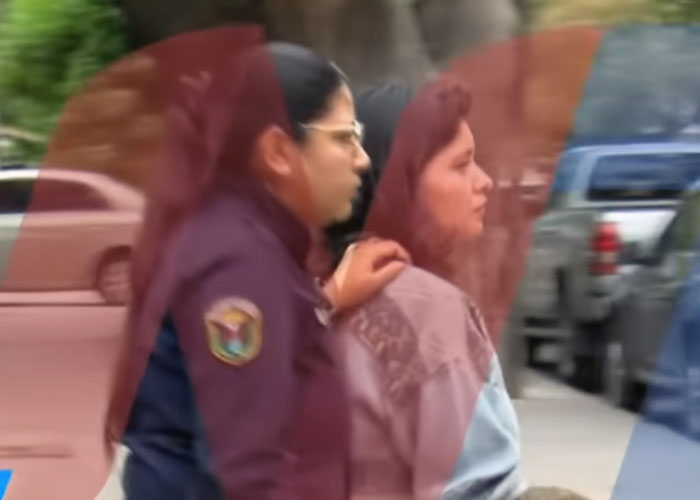 Woman accused of giving anti-anxiety medication to her 9-year-old daughter, escorted by a female officer outdoors.
