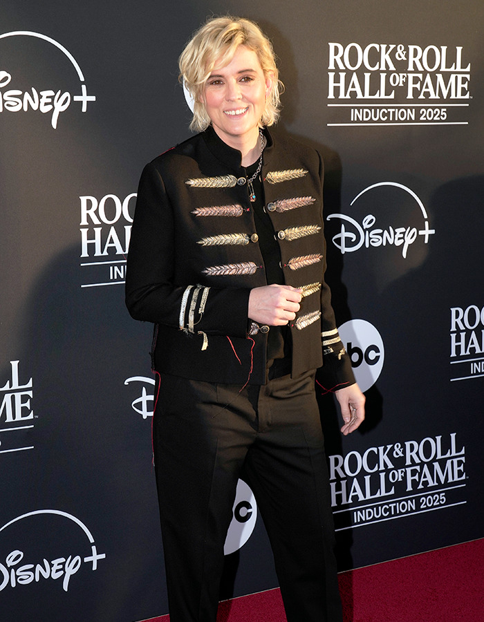 Chappell Roan smiling in a black decorated jacket and pants at the Rock Hall of Fame 2025 red carpet event.