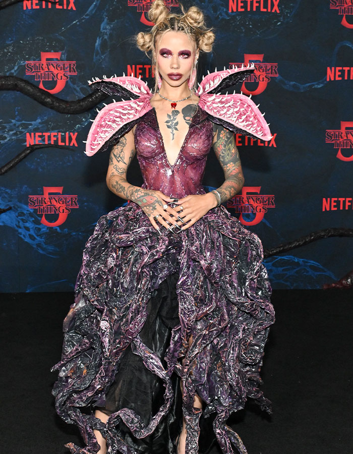 Person with elaborate purple and black dress and winged shoulder pieces at Stranger Things 5 red carpet premiere.