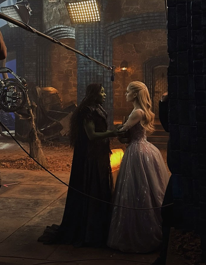 Ariana Grande and Cynthia Erivo in character on set during filming, preparing for a scene in a medieval setting.