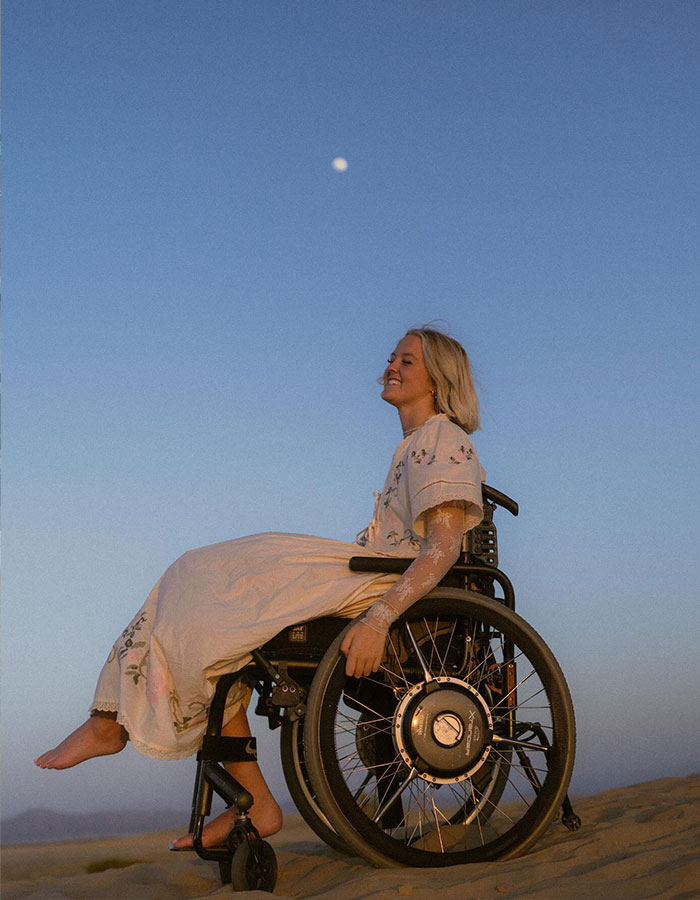 Young girl in a wheelchair outdoors at sunset, representing the story of a girl paralyzed after a basic mistake during a fun adventure.
