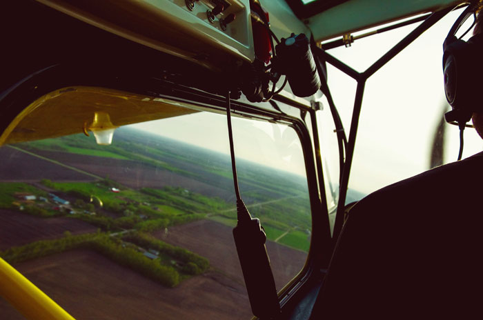 View from inside a small aircraft cockpit showing a pilot's silhouette and the landscape during mid-flight close calls.