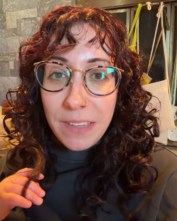 A woman with curly hair and glasses discusses romantasy books and reactions to controversial author comments.