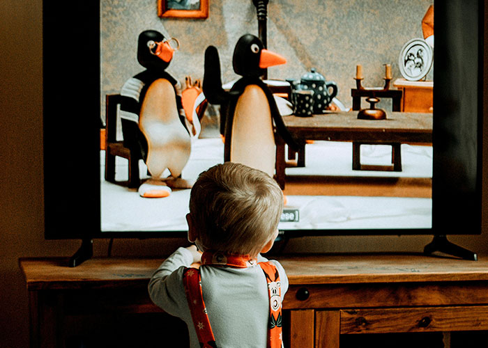 A child watching penguin characters on a TV screen, illustrating people sharing life hacks for everyday use.
