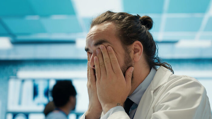 Tired dad rubbing eyes in a medical setting, showing lovable clueless dads moments during pregnancy.