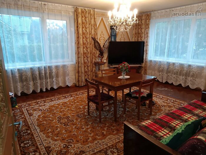 Cozy vintage living room with floral curtains, wooden furniture, patterned carpet, and a chandelier in real estate listing photos.