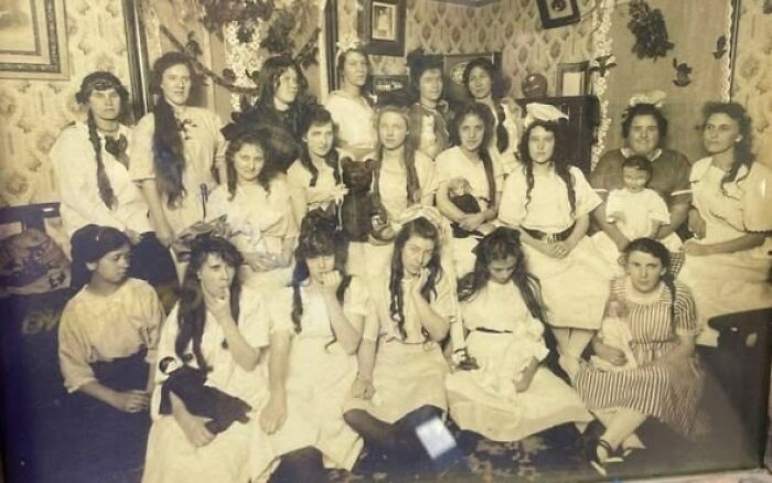 Group of young women and girls dressed in Victorian-Edwardian clothing posing indoors in a vintage sepia-toned picture.