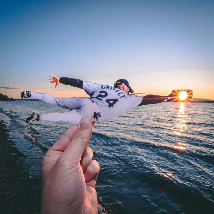 Hand holding a paper cutout of a baseball player diving to catch the sun over water, showing brilliant paper cutouts art.