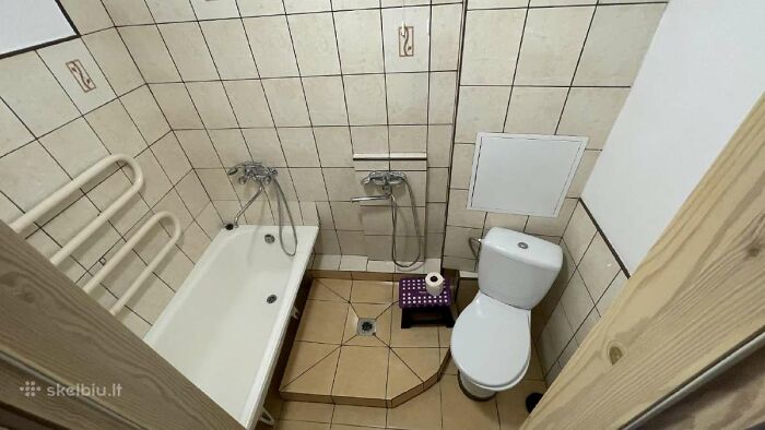 Small bathroom with bathtub, toilet, and shower setup in a tight space, featured in wild real estate listings.
