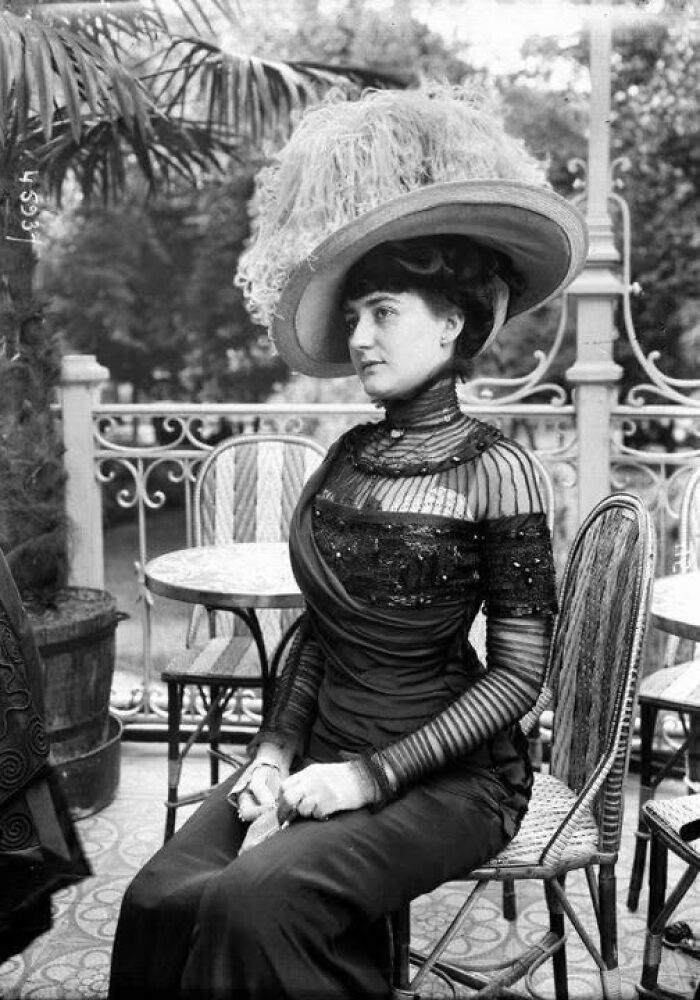 Victorian Edwardian pictures of a woman seated outdoors wearing a large feathered hat and elegant dress from the early 1900s.