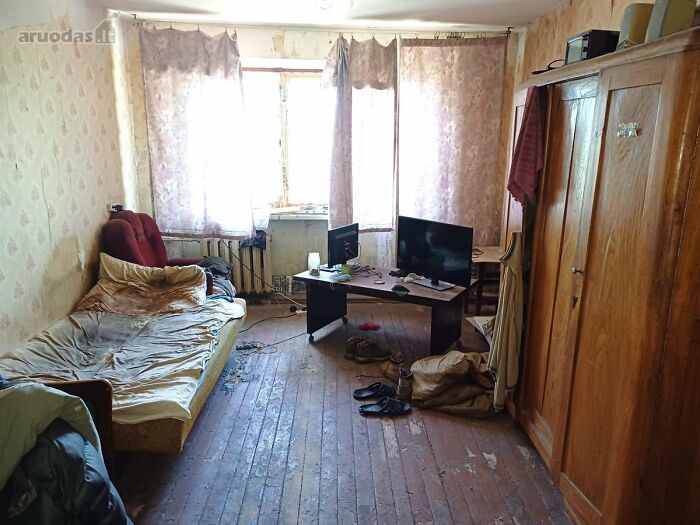 Habitación modesta con muebles básicos, sofá viejo y escritorio con computadora en listado de bienes raíces entretenido.