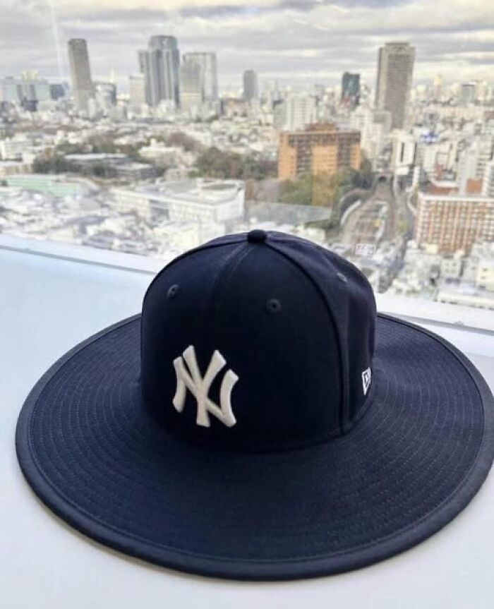 Black New York Yankees hat with an extra-wide brim placed on a windowsill overlooking a cityscape.